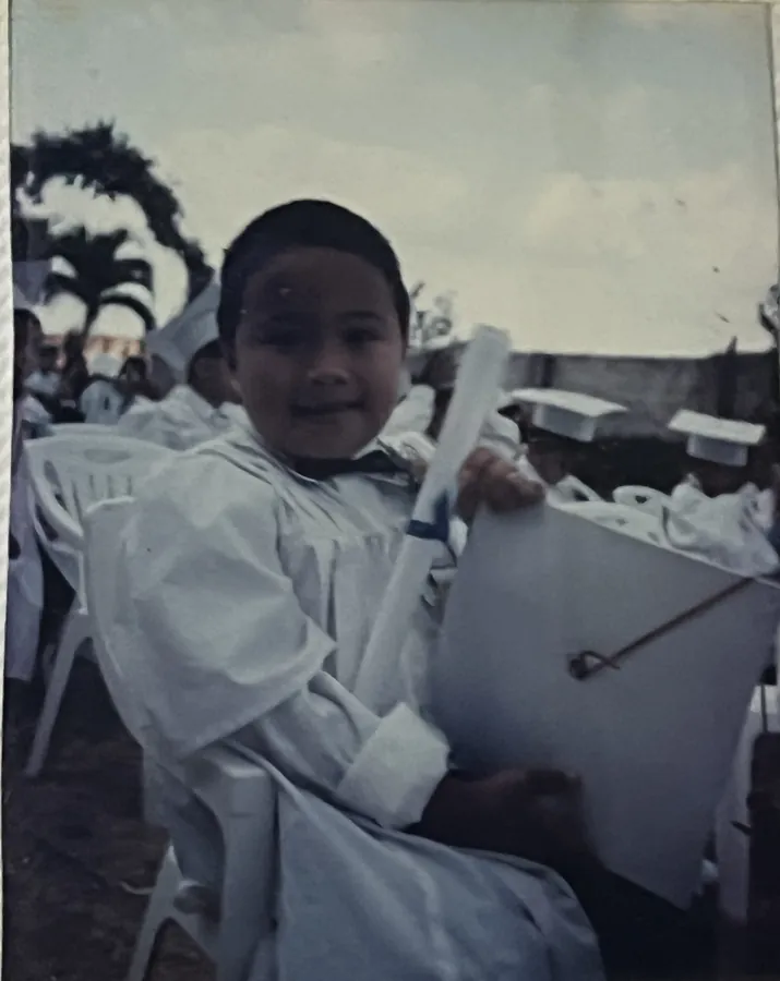 Ian in a white graduation gown, holding his diploma