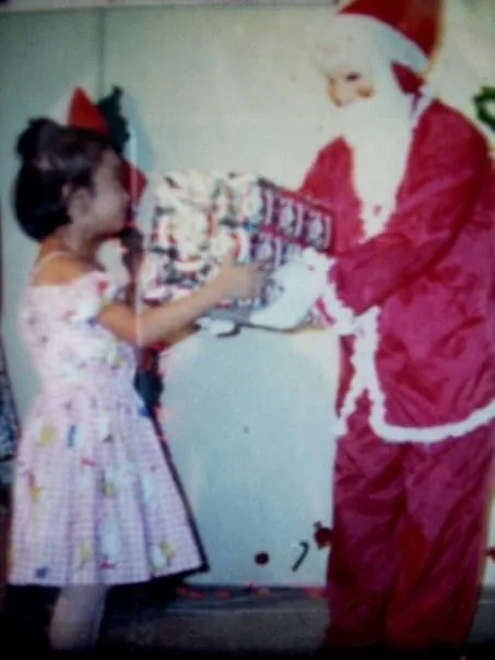 Merce as a girl handing Santa a present